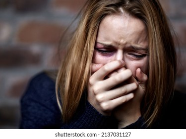 Emotionally victimized. Abused young woman crying hard and covering her mouth.
