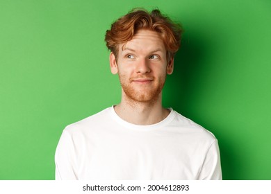 Emotions And Fashion Concept. Close-up Of Handsome Redhead Male Model With Beard And Messy Haircut, Looking Left And Smiling, Green Background