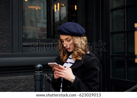 emotions, people, beauty and lifestyle concept - Girl Frenchwoman. Street photo of young woman wearing stylish classic clothes. Female fashion concept. French style. Girl texting on the smart phone