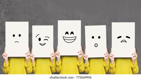 Emotions set. Girl hiding face behind signboard with drawn smileys. Collage of indifferent, winking, happy, surprised, and sad emoticons.