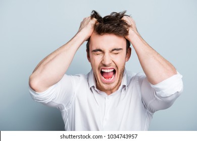 Emotions, stress, madness and people concept - crazy shouting man rending his hair in white shirt, screaming with close eyes and wide open mouth, holding hands on head over gray background