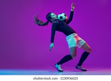 Emotive girl, female soccer, football player in motion, action isolated on purple studio background in neon light. Concept of sport, action, motion, fitness, team, achievements and goals