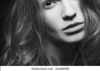 Emotive Portrait Of A Young Beautiful Girl With Curly Long Hair Posing Over Black Background. Perfect Skin And Hair. Spa Salon. Close Up. Black And White (monochrome) Studio Shot