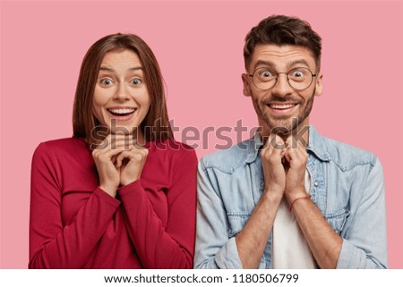 Emotive teenagers keep hands together have positive facial expressions, anticipate something wonderful, pose together against pink background. People, relationship, emotions, lifestyle concept