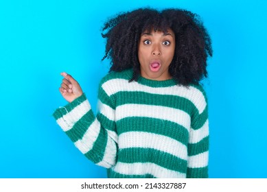 Emotive Young Woman With Afro Hairstyle Wearing Striped Sweater Over Blue Background Keeps Jaw Dropped From Shock Demonstrates Amazing Promo Points Right On Blank Space Demonstrates Big Shopping Sal