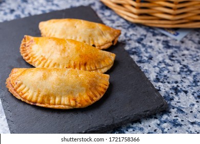 Empanadillas or spanish small pasties on a squared blackboard plate on a kitchen blue granite background with basket. Spanish traditional food and tapas with negative space.