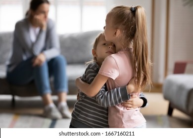 Empathic elder sister cuddling comforting little brother, while stressed annoyed mother sitting on couch at home. Small children siblings supporting each other after family quarrel with mum. - Powered by Shutterstock