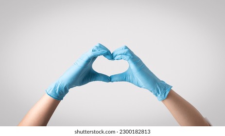 Emphasizing compassion in healthcare. Woman doctor wearing protective gloves, forming a heart shape with her hands, symbolizing the vital role of empathy in providing high-quality patient care - Powered by Shutterstock