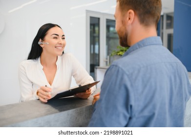 The Employee Of The Beauty Salon Meets The Client In The Reception Of A Modern Beauty Salon. A Man Signs A Paper With The Consent For Maintenance. The Woman Smiles At Him.