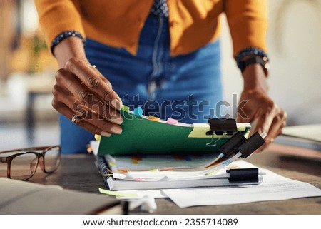 Employee black woman hands working on stacks of workpaper files and searching for unfinished documents. African american secretary holding and arranging stack of business documents and folders.