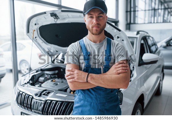 Employee in the blue colored uniform stands in the\
automobile salon.