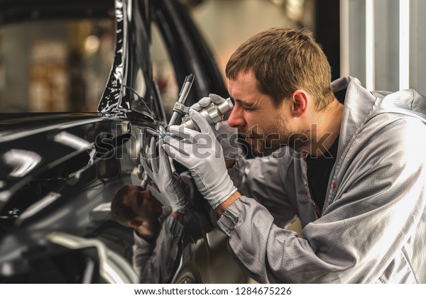 Employee car body painting shop checks\
the quality of the painted surface using a\
microscope