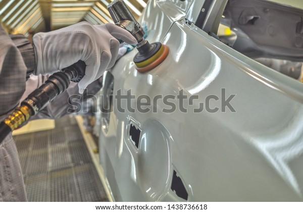 An employee of the car\
body painting shop polishes the painted surface with a pneumatic\
polishing machine