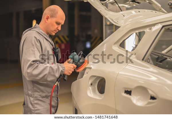 An employee of the car\
body painting shop polishes the painted surface with a pneumatic\
polishing machine