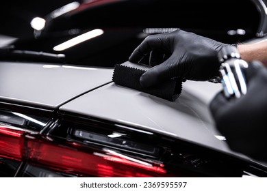 Employee of a car detailing studio or car wash applies a ceramic coating to the paint of a gray car