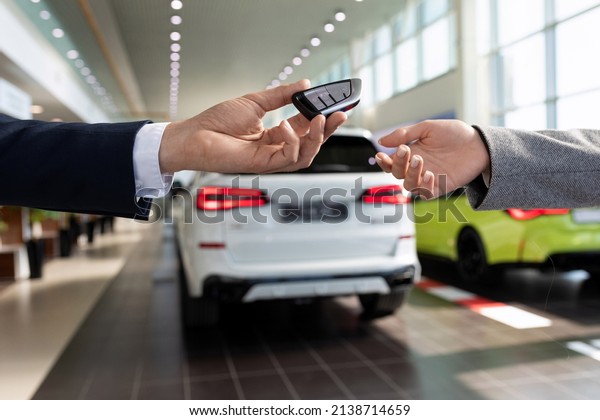 an\
employee of a car store handing over the keys to a new car to a\
buyer close-up against the backdrop of the\
showroom
