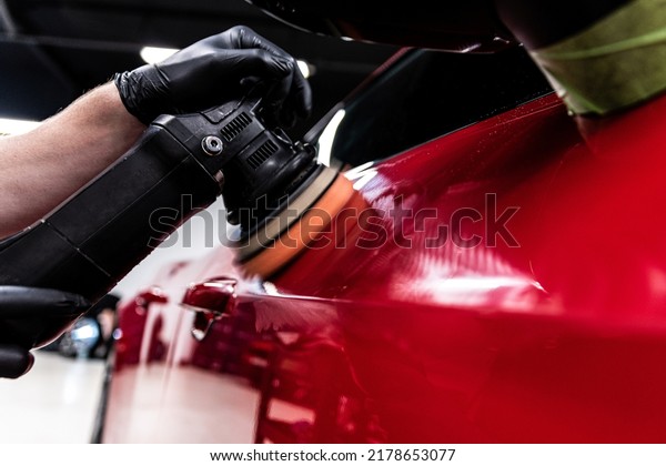 Employee of a car wash or a car detailing studio\
polishes the car paint