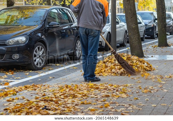 An employee\
in the city sweeps leaves from the sidewalk into a pile in the\
fall. Panevezys Lithuania 23 October\
2021