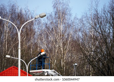 An employee of an electrical network is changing a light bulb on a column of outdoor street lighting