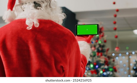 Employee in festive ornate shopping mall wearing Santa Claus suit holding green screen phone, taking a break from job shift and watching videos on chroma key screen, close up - Powered by Shutterstock