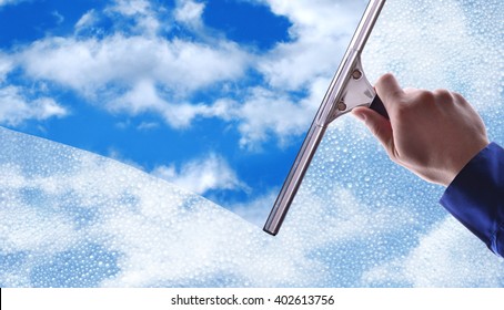 Employee hand cleaning a glass with rain drops and blue sky background.Concept and background window cleaning. horizontal composition