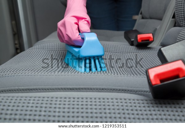 Employee hand in rubber protective glove cleaning\
textile back seat with professionally brush. Early spring regular\
cleanup. Care about auto interior. Commercial cleaning company\
concept. Front view.