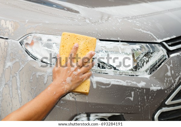 employee hand washing car light with yellow sponge\
in car wash shop.