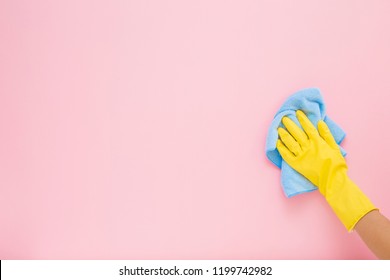 Employee hand in yellow rubber protective glove wiping pastel pink wall from dust with blue dry rag. General or regular cleanup. Commercial cleaning company. Copy space. Empty place for text or logo. - Powered by Shutterstock