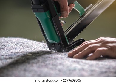 An employee holds in his hands an industrial air stapler for sheathe soft fabric upholstery. Close-up. Manufacture of upholstered furniture
