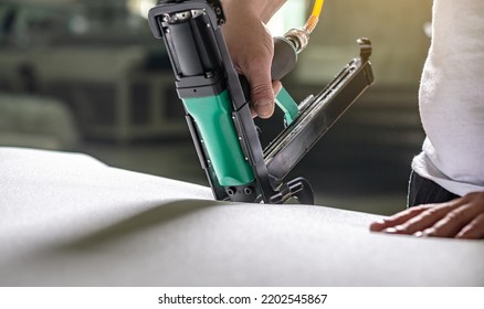 An employee holds in his hands an industrial air stapler for sheathe soft fabric upholstery. Close-up. Manufacture of upholstered furniture - Powered by Shutterstock