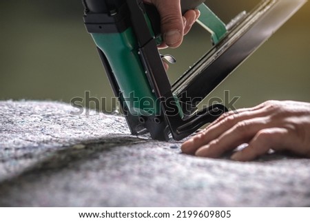 An employee holds in his hands an industrial air stapler for sheathe soft fabric upholstery. Close-up. Manufacture of upholstered furniture