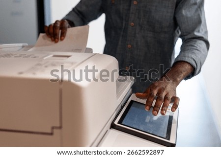 Employee operating a multifunction printer, making photocopies and managing various print jobs in a busy office environment