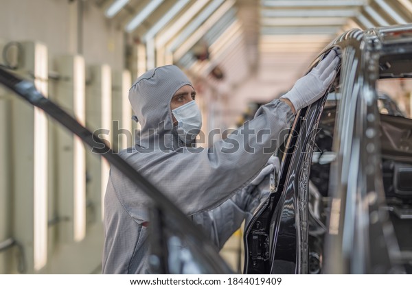 An employee of the paint shop of an\
automobile factory in a medical mask on his face checks the quality\
of the painted surface. Working during a\
pandemic