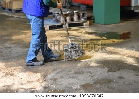 The employee performs floor cleaning at the factory. The worker sweeps floors in the factory filled with special sand to remove industrial dirt
