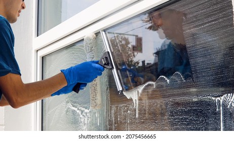 An employee of a professional cleaning service in overalls washes the glass of the windows of the facade of the building. Showcase cleaning for shops and businesses - Shutterstock ID 2075456665