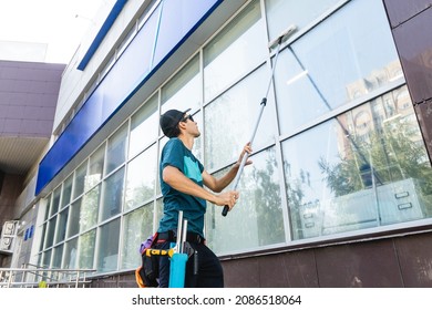 An employee of a professional cleaning service in overalls washes the facade and windows with special devices