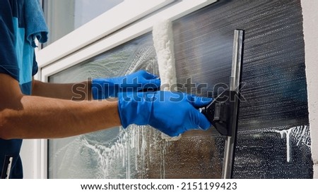 An employee of a professional cleaning service in overalls washes the glass of the windows of the facade of the building. Showcase cleaning for shops and businesses.