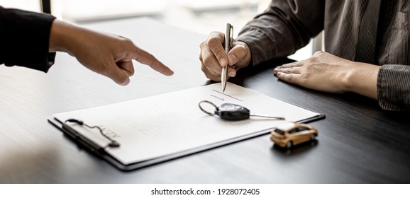 An employee of the rental car company points to the contract document in the Renter's signature box to have the tenant sign the rental agreement to agree to the rental agreement. Concept car rental.