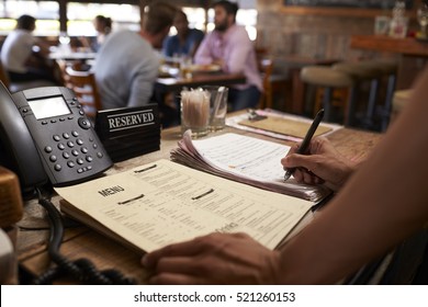 Employee At A Restaurant Writing Down A Table Reservation