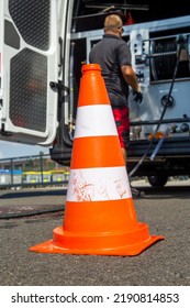 Employee Of A Sewer Cleaning Company Cleaning A Street Drain. In The Foreground, The Construction Site Cap, In The Background, The Emergency Vehicle