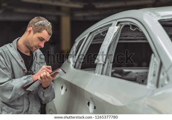 Employee in the shop painting the\
car body writes a mark on the defects production defect\
maps