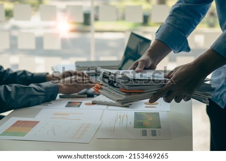 An employee sits at a table full of paper. stamp on the pile of unfinished documents A young account manager's secretary works in the office among piles of paperwork on the table.