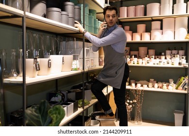 An Employee Of A Souvenir And Gift Wrapping Store Is Looking For A Box On The Rack While Talking On The Phone