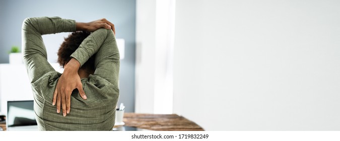 Employee Stretching At Office Desk At Work