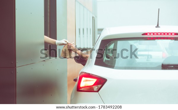 Employee wearing\
gloves delivers take out food out the window. Shopping for food\
from the car. Pick up fast food from the counter. Concept of social\
distance and new\
normality.