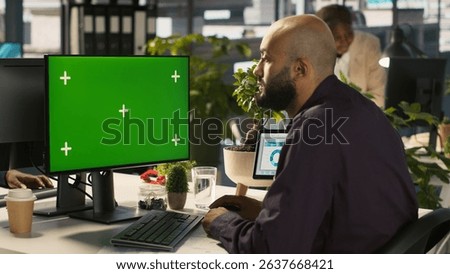 Employee at work using isolated screen PC to check progress done on customer commissioned project. Office clerk in front of mockup computer reading data statistics on paperwork after audit, camera A