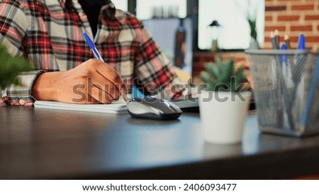 Employee working from home cross referencing information, transcribing data from computer to notebook. Teleworker remotely working in warm cozy stylish home, typing and writing, close up