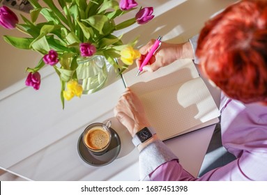 An employee writes in the notebook. Coffee cup at office work place. Home working - Shutterstock ID 1687451398