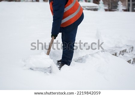 Employees of municipal services in a special form are clearing snow from the sidewalk with a shovel.
