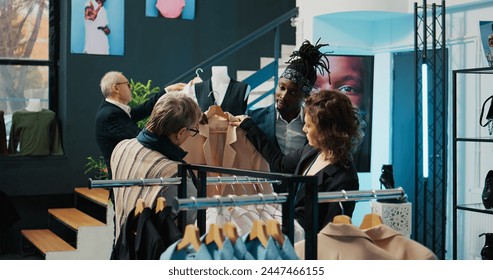 Employees team presenting variety of clothes to senior client, helping her to choose the perfect shirt size to create a formal outfit. Diverse store assistants show clothing from designers. Camera B. - Powered by Shutterstock